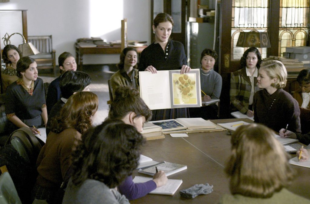 A person holding a book in front of a group of people
Description automatically generated
